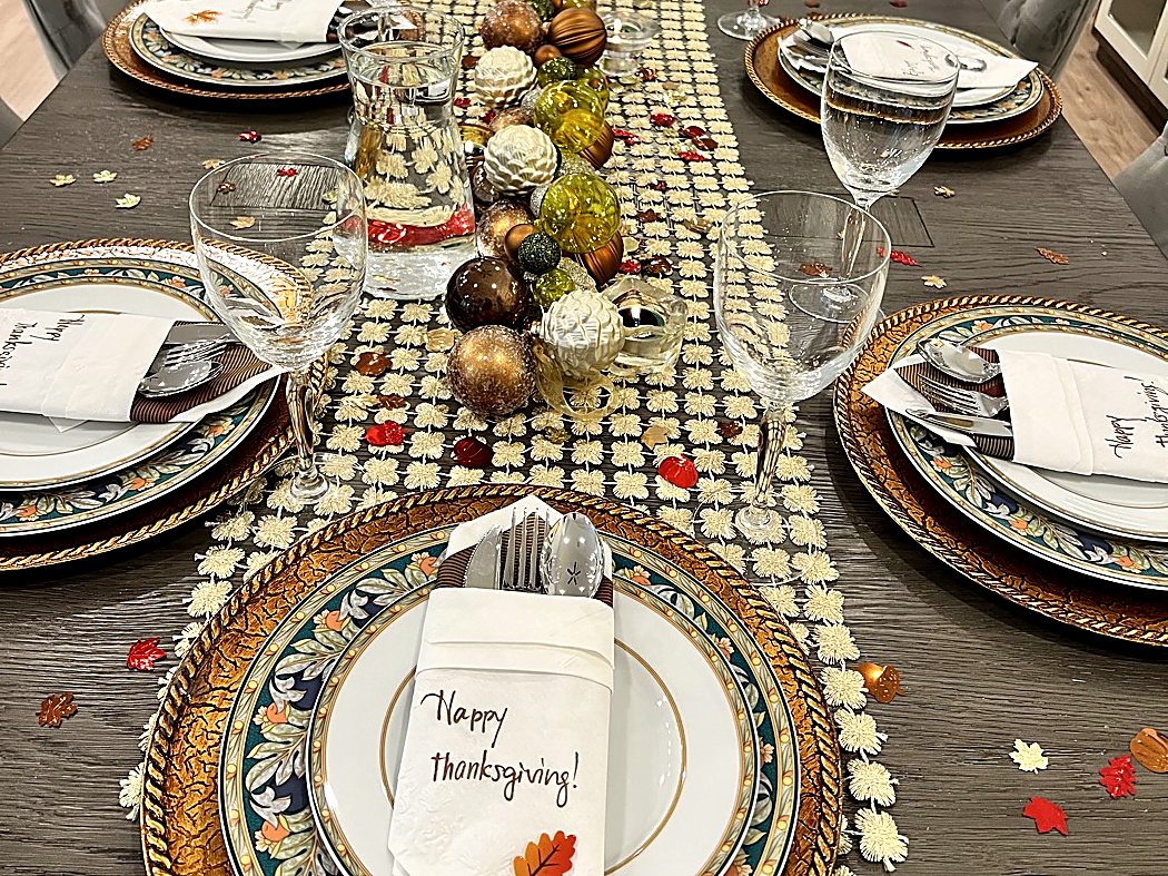 A long Thanksgiving table set with gold chargers, patterned china, and hand-written napkin cards.